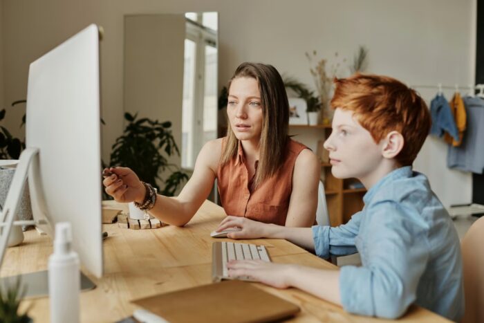 A mother and her son attentively engaged in online learning at home on a computer. A mother and her son attentively engaged in online learning at home on a computer.