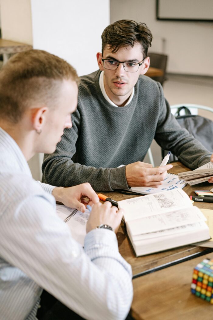 pexels-photo-5676678-5676678 Two young men studying together at a table with books and notes.