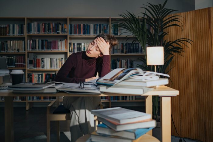 pexels-photo-8086357-8086357 A tired woman surrounded by books, studying in a library, feeling overworked and stressed.